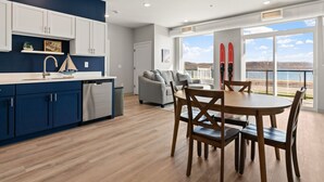 A modern kitchen with white cabinets, a stainless steel dishwasher, and a dining area with a wooden table and chairs.