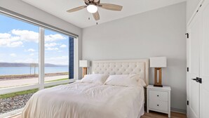 Un dormitorio con una ventana grande, una cama, una mesita de noche y un ventilador de techo.