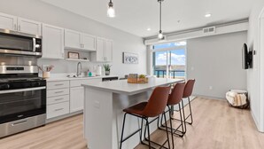Cocina moderna con armarios blancos, una isla grande con taburetes altos, electrodomésticos de acero inoxidable y vistas al exterior.