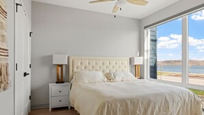Ein Schlafzimmer mit einem großen Bett, zwei Nachttischen, einem Deckenventilator und Seeblick durch große Fenster.