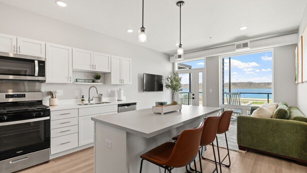 A modern kitchen with white cabinets, a large island, and a view of the outdoors. - Condo with stunning views of Lake Pepin Unit 104 (Lake City)