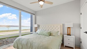 A bedroom with a large window, a bed, a nightstand, and a ceiling fan. - Condo with stunning views of Lake Pepin Unit 104 (Lake City)