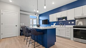 A modern kitchen with a blue accent wall, white cabinets, a central island with bar stools, a built-in oven, and pendant lighting.