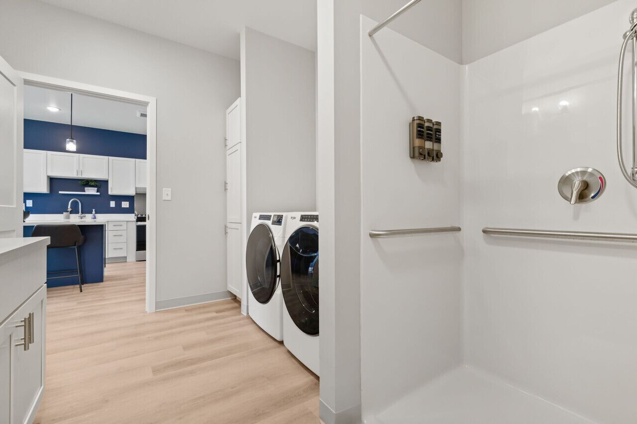 A modern apartment with a kitchen, a laundry area, and a shower.