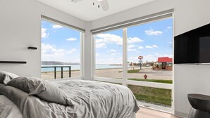 Ett sovrum med en stor säng, en tv och utsikt över en strand och en väg.