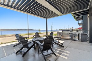 An outdoor patio with Adirondack chairs, a round table, and a grill area overlooking a body of water.