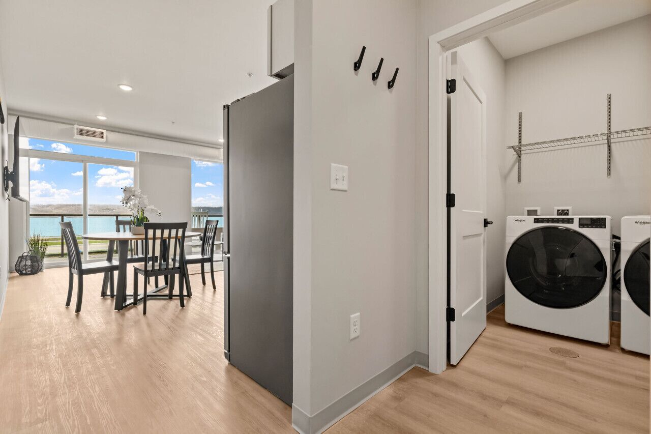 A modern apartment with a dining area, a gray refrigerator, a washing machine, and a view of the sea.