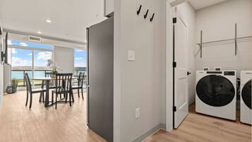 A modern apartment with a dining area, a gray refrigerator, a washing machine, and a view of the sea.