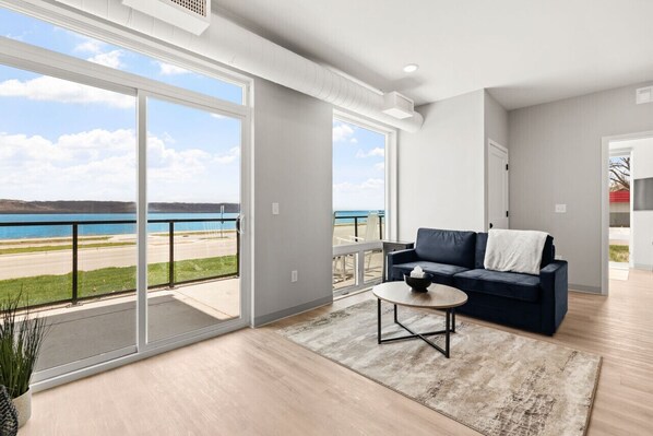 A spacious living room with a large sliding glass door leading to a balcony with a view of the beach and ocean.