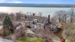 Uma casa grande de dois andares com uma chaminé notável, uma pequena varanda e vista para um lago.