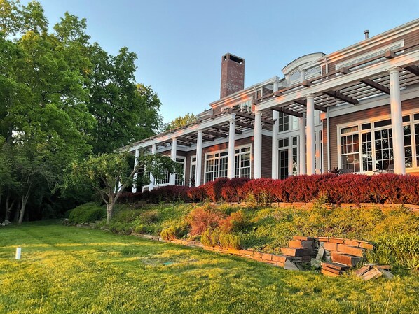 A modern building with a covered patio area, large windows, and a well-maintained garden with various plants and a brick pathway.