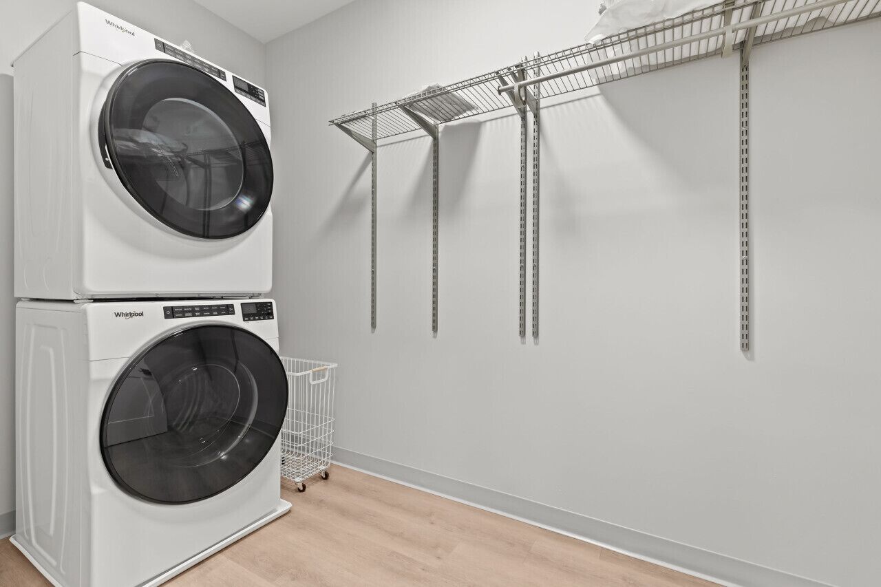 Une buanderie équipée de deux lave-linge Whirlpool superposés et d’un étendoir métallique.