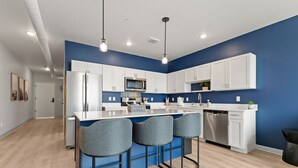 A modern kitchen with white cabinets, a central island with bar stools, and a blue accent wall.