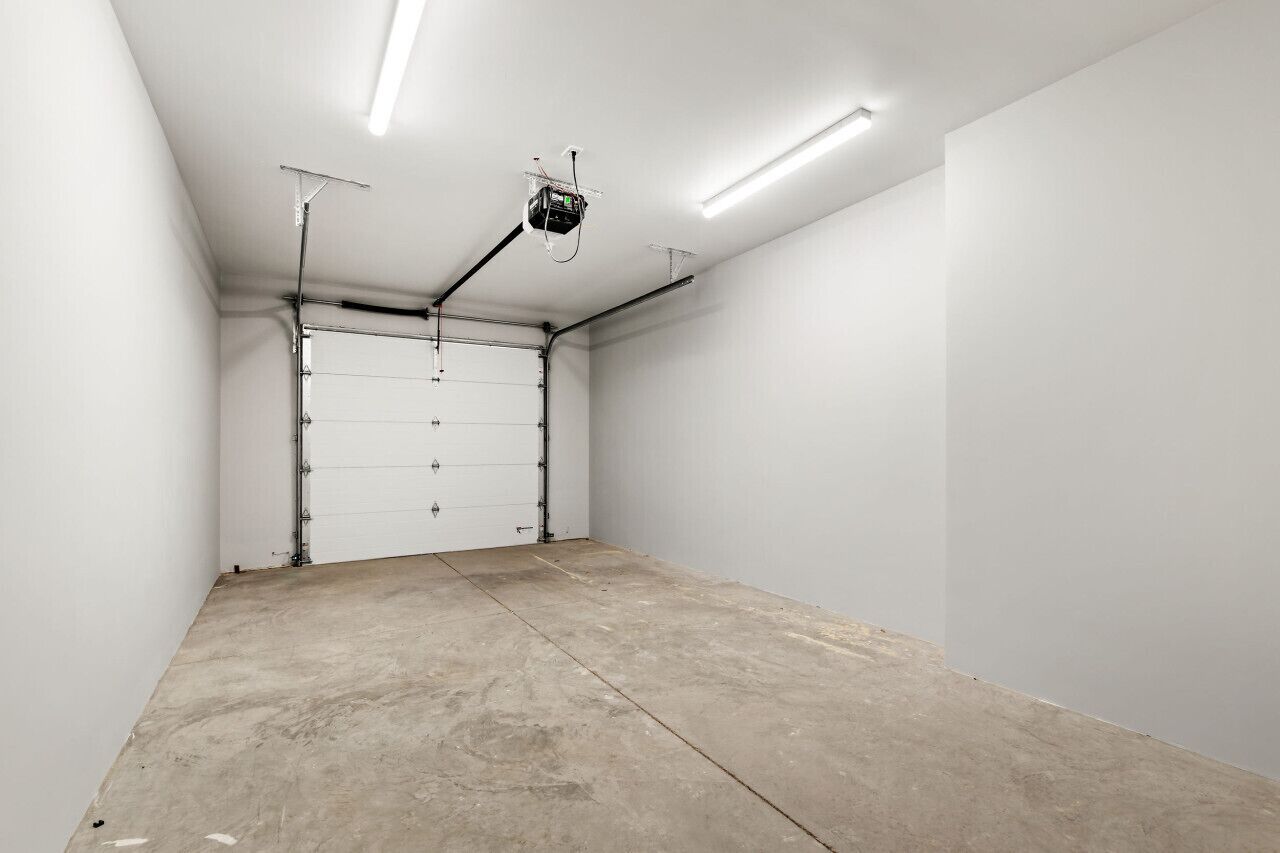 A clean, empty garage with white walls, a concrete floor, and fluorescent lighting.