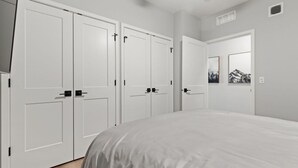 A bedroom with a large bed, white wardrobes, and a door with a mountain painting.