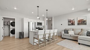 Una cocina moderna con armarios blancos, una isla central con taburetes de bar, un microondas y un refrigerador.