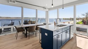 Et moderne køkken med en stor ø, et spiseområde med stole og store vinduer med udsigt over en sø.
