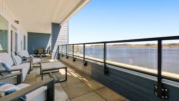 A balcony with a view of a lake, furnished with a sofa, chairs, and a small table.