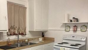 A kitchen with white cabinets, a sink, a stove, and a blue mat on the floor. - Charming 2-bedroom townhome in quaint Hamlet with WiFi, AC (Hamlet)
