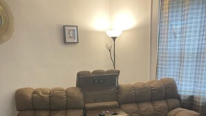 A living room with a large, tufted sofa, a small table with a cup, a lamp, and a framed picture on the wall. - Charming 2-bedroom townhome in quaint Hamlet with WiFi, AC (Hamlet)