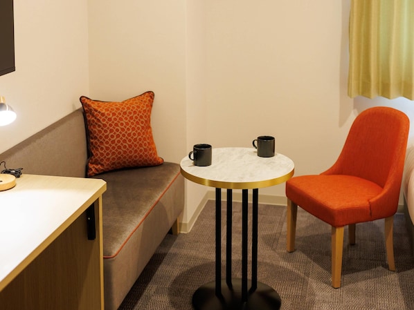 A small, cozy room with a sofa, a round table, and a single orange chair. - Comfort Hotel Kii Tanabe (Tanabe)