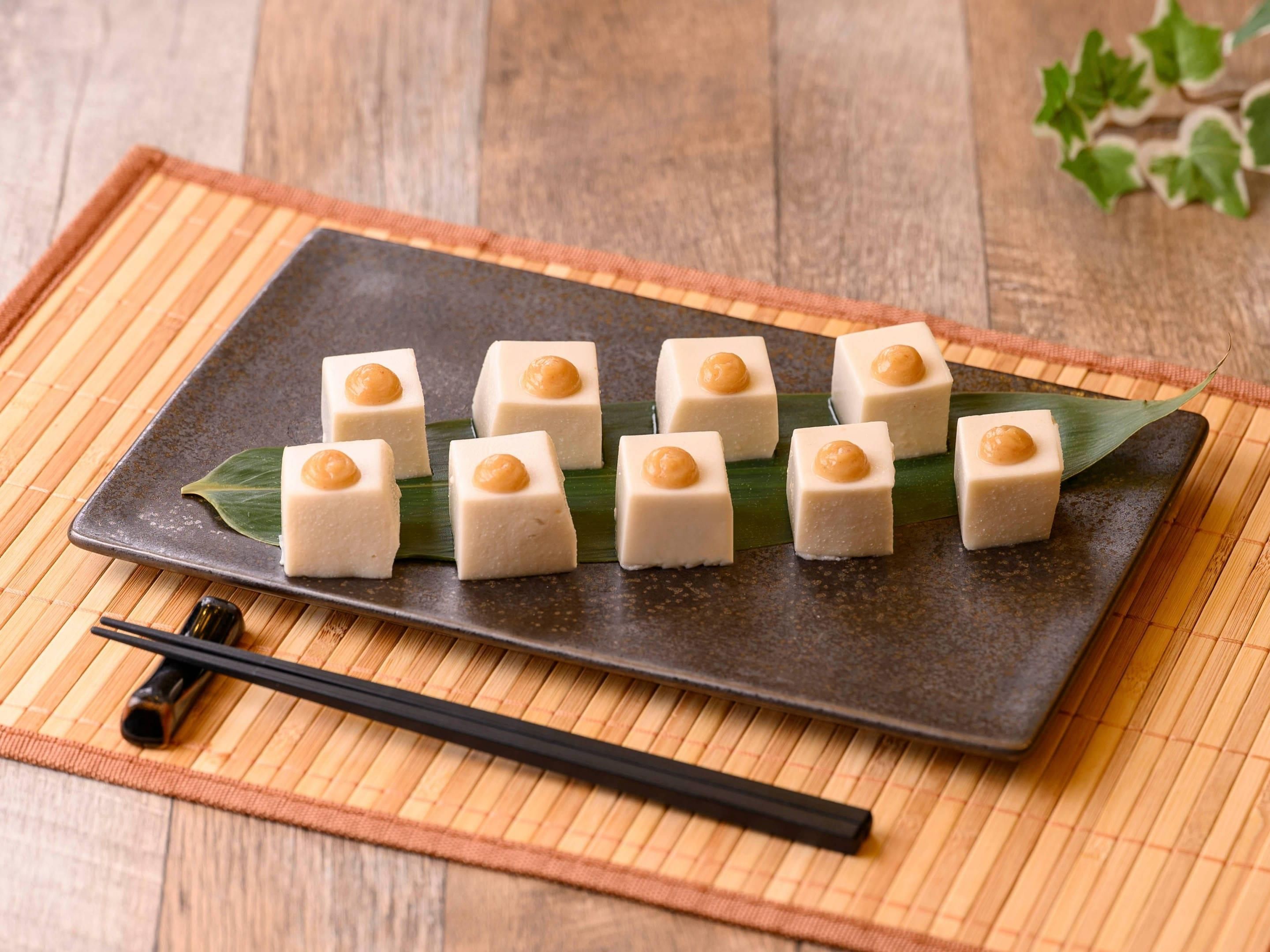 A rectangular plate with square-shaped food items, each topped with a round, golden-brown object, placed on a bamboo mat.
