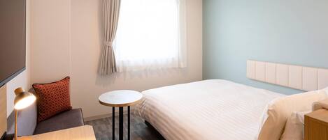 Une chambre d’hôtel avec un lit, une petite table ronde, une lampe, un canapé et une fenêtre avec des rideaux.