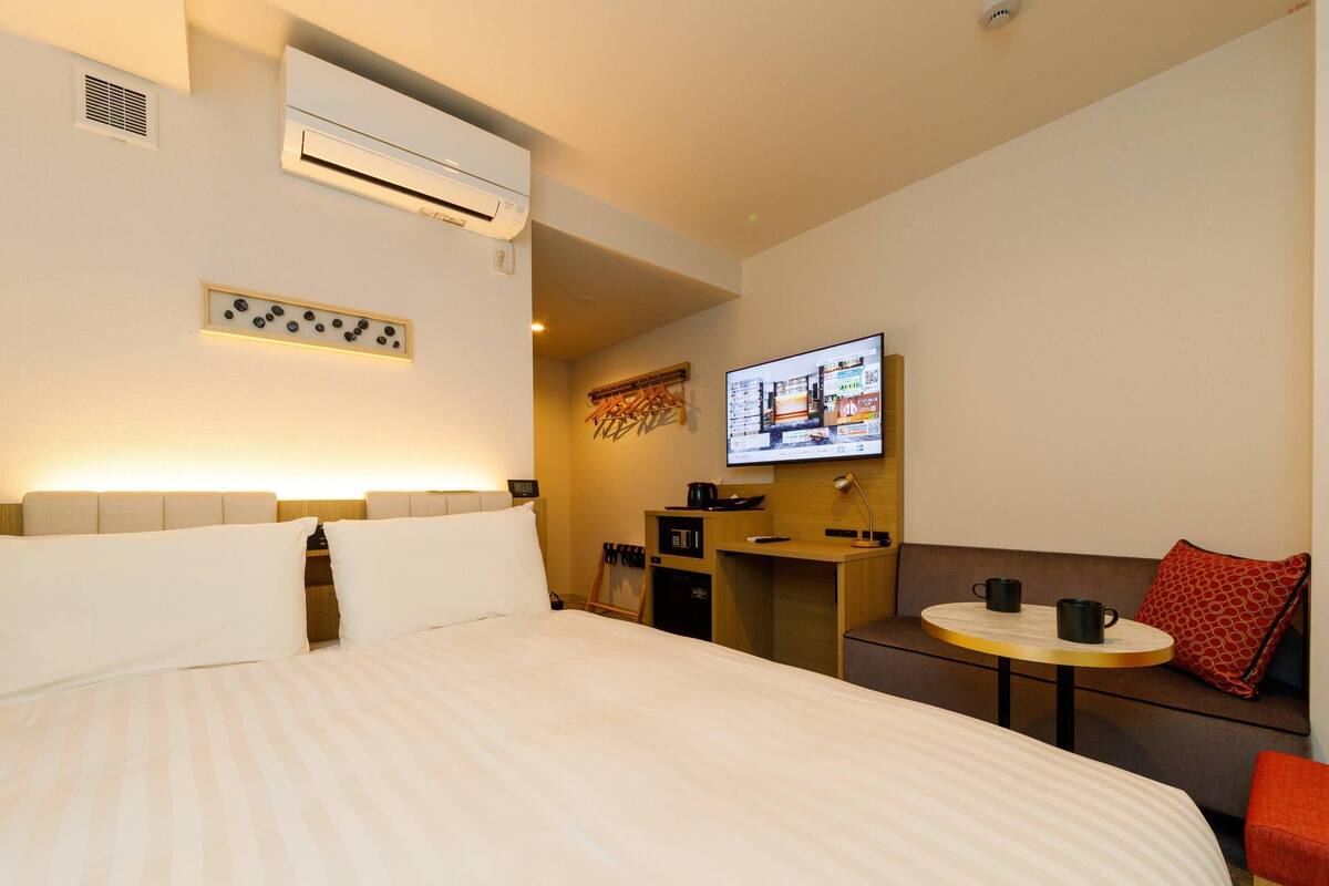 Una habitación de hotel con una cama grande, un escritorio, un televisor y una mesita con dos tazas.