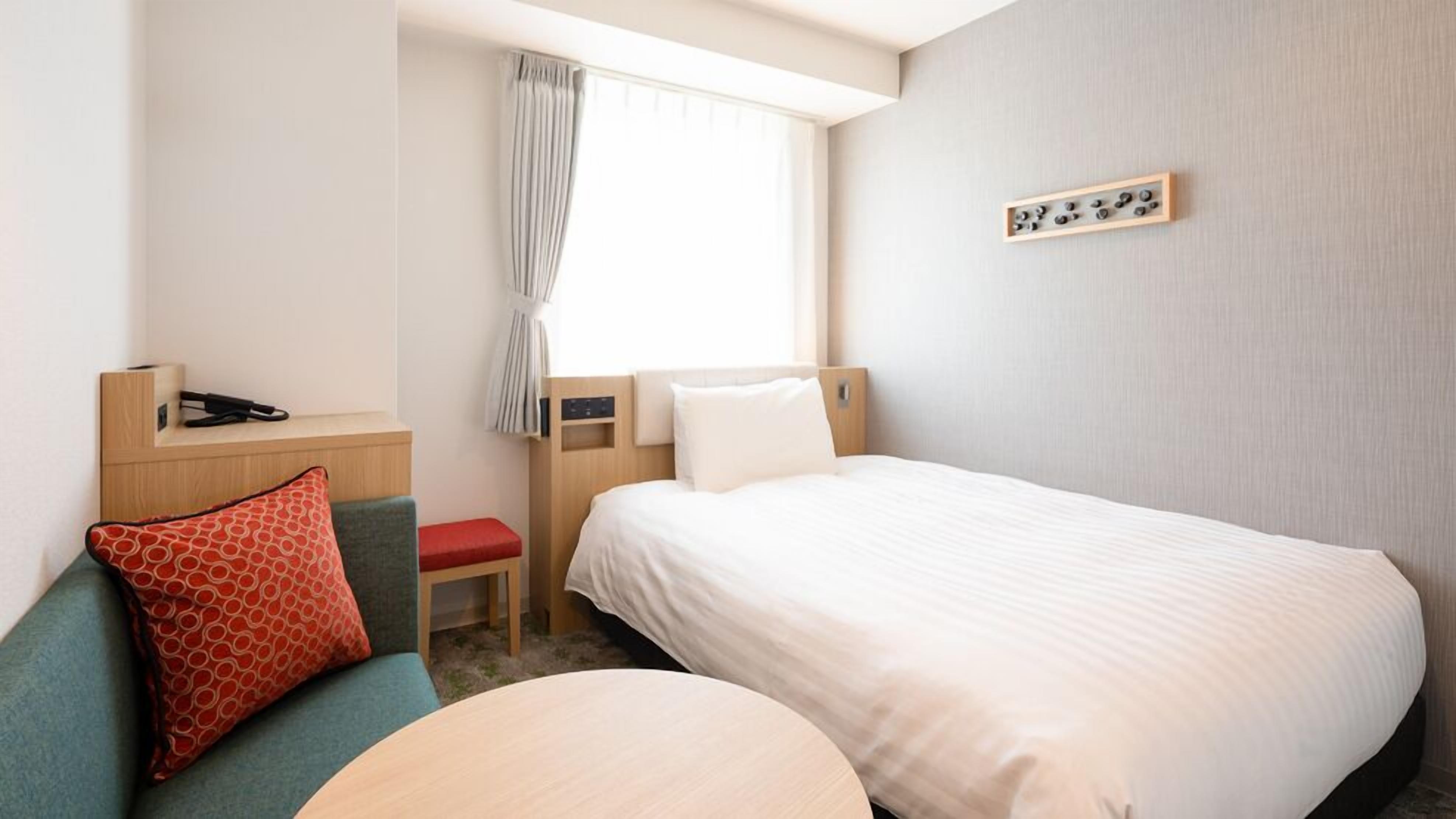 Ein Hotelzimmer mit einem Bett, einem Schreibtisch, einem Stuhl, einem kleinen Tisch und einem Fenster mit Vorhängen.
