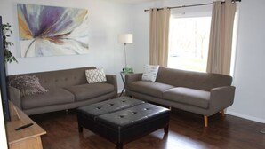 A living room with two sofas, a black ottoman, a floor lamp, and a painting on the wall. - Charming & Secluded Farm House (Somerset)