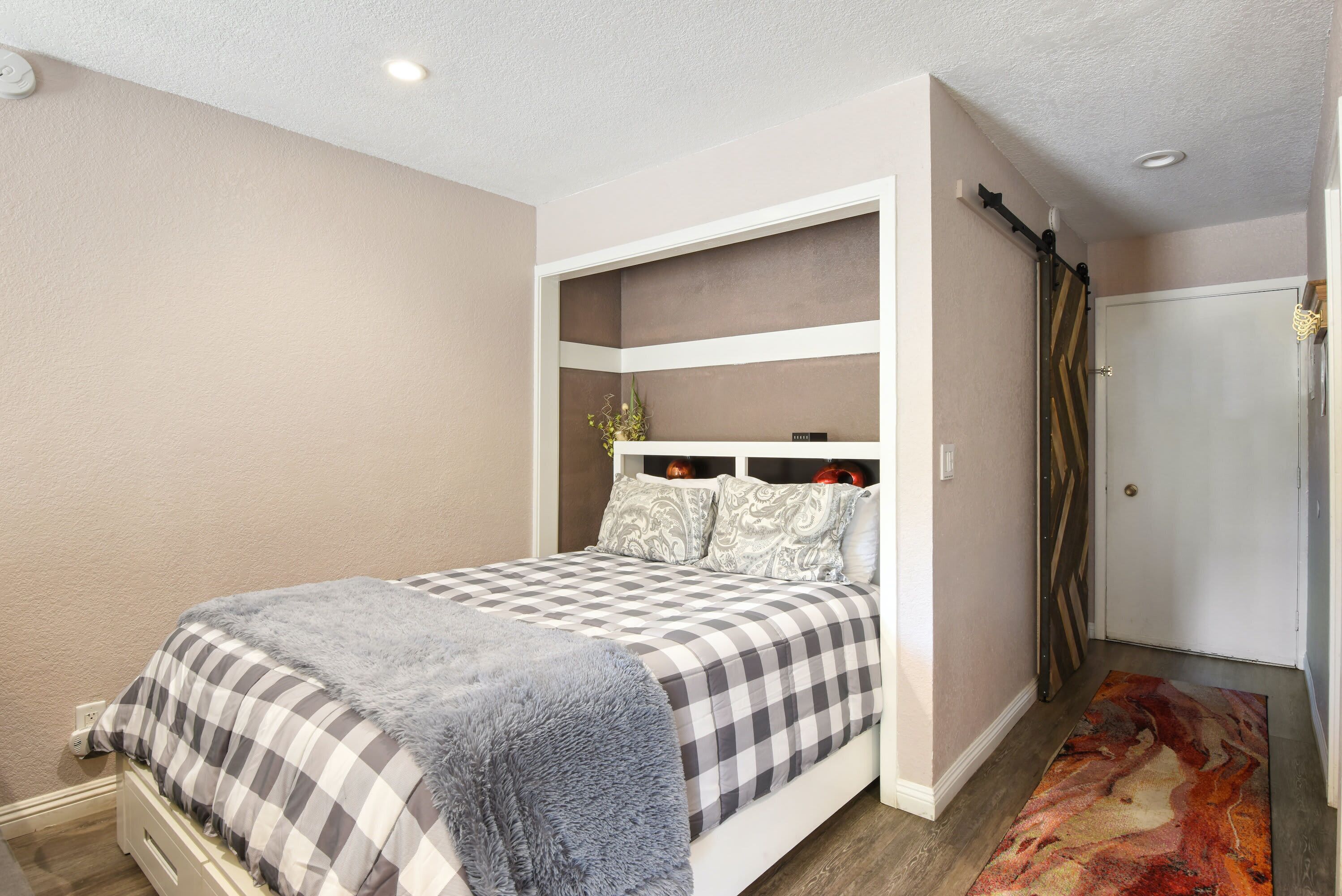 A bedroom with a bed, a built-in bench, a door, and a patterned rug.