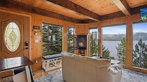 A cozy cabin interior with a fireplace, wooden walls, and large windows overlooking a lake. - Stunning Views at Stargazer | Lakefront Studio! (Crystal Bay)