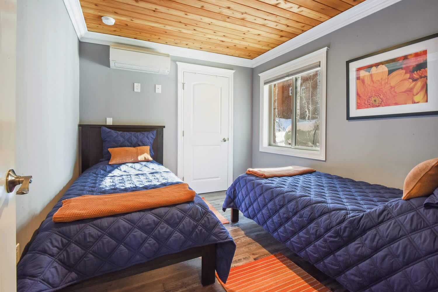A bedroom with two beds, a wooden ceiling, a window with a view, and a door.