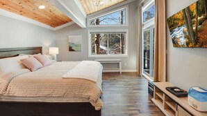 A bedroom with a large bed, a bench, a desk with a computer, and a painting. - Alpine Chalet – Nature Lovers Rejoice! Chic 4 BDR (Alpine Meadows)
