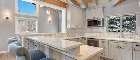 A modern kitchen with white cabinets, a marble countertop, and wooden beams on the ceiling.