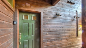 A wooden door with a green handle and a keyhole, a metal doorbell, and a small mailbox on the wall.