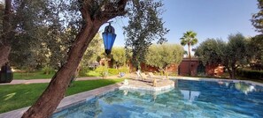 A swimming pool with a tiled deck, surrounded by greenery and a palm tree. - DAR HISANE (Oulad Hassoune)