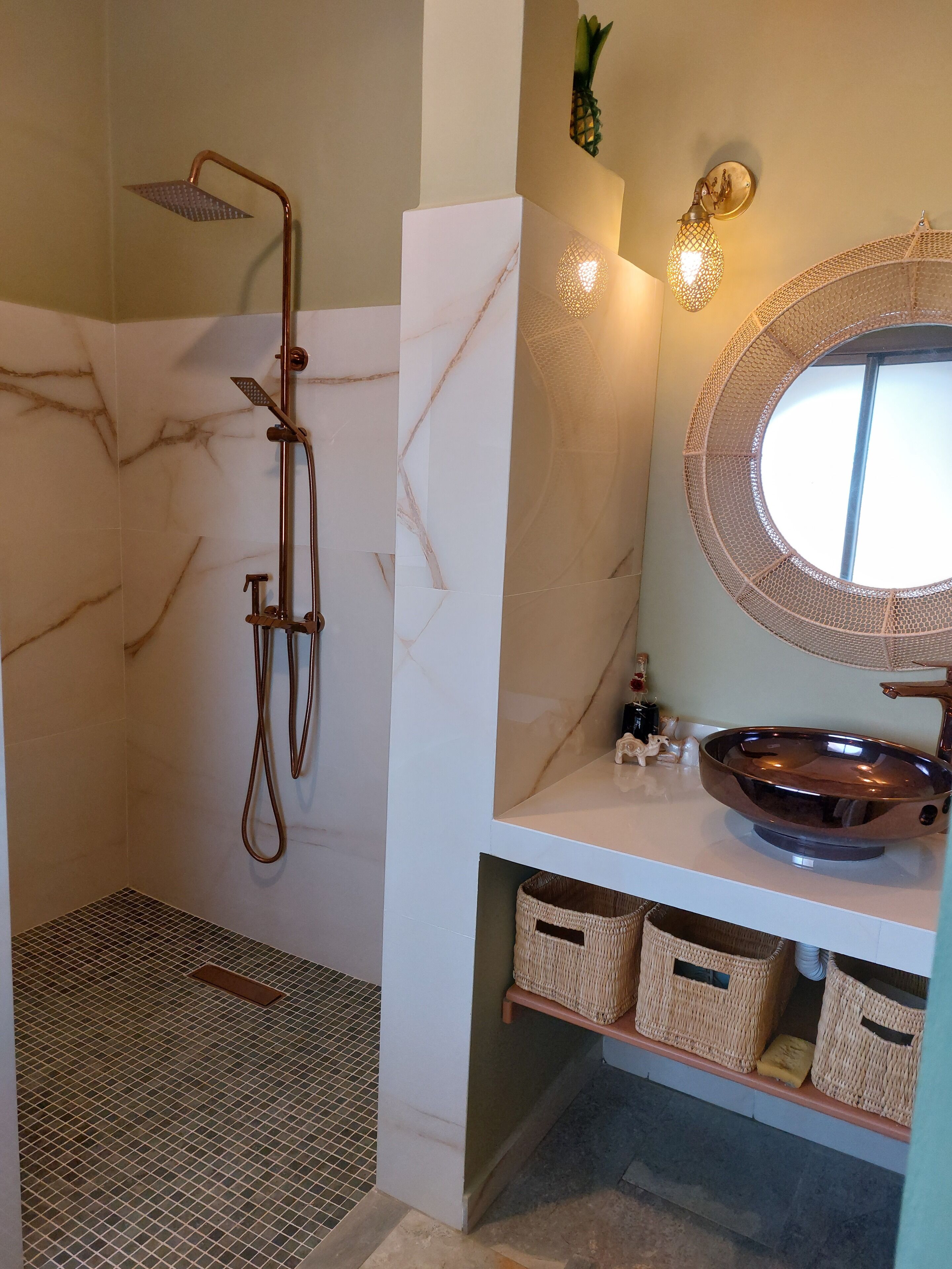 A bathroom with a shower, a marble wall, a round mirror, and a sink with a vessel basin.
