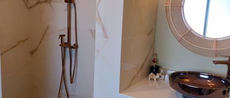 A bathroom with a shower, a marble wall, a round mirror, and a sink with a vessel basin.