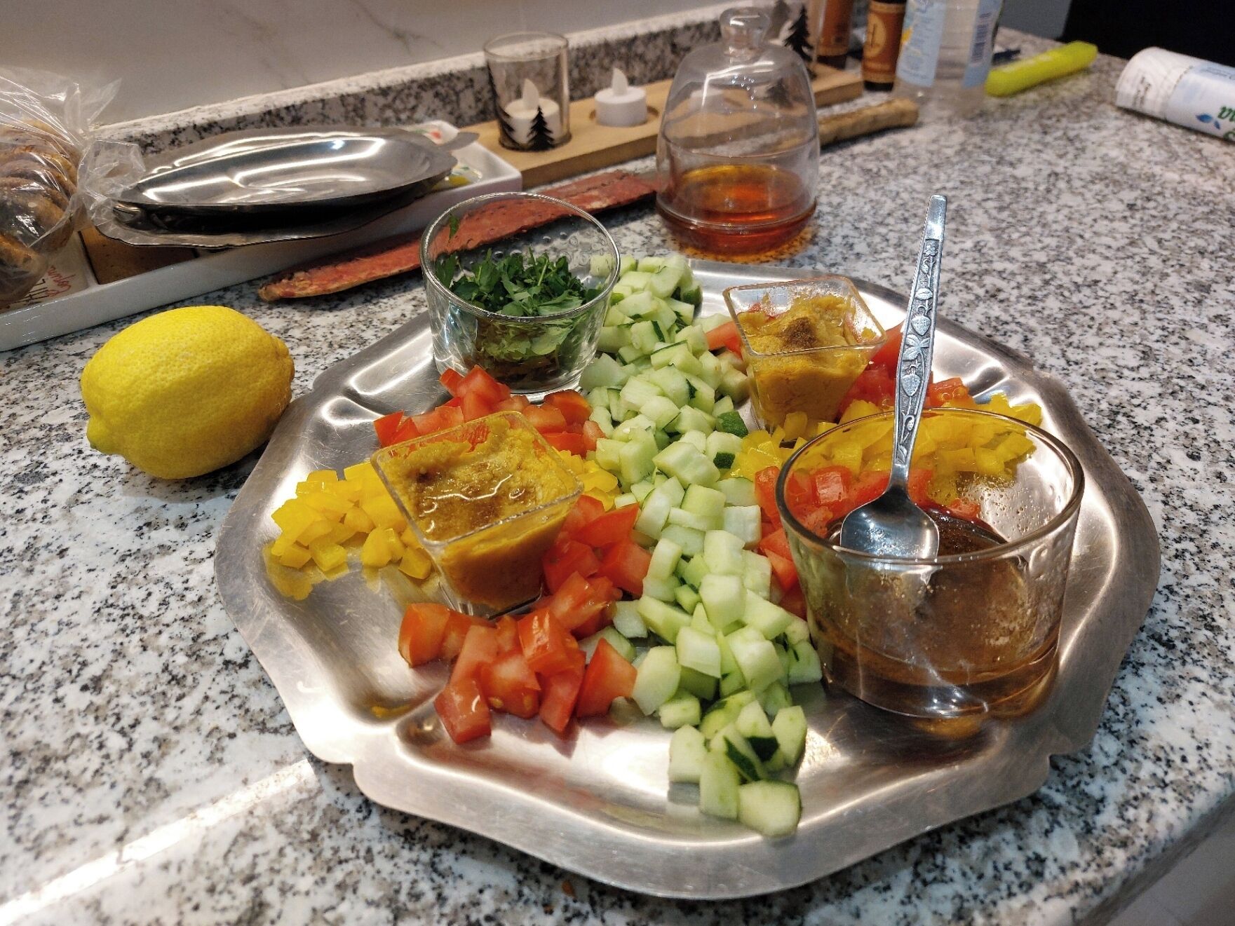 A stainless steel tray with various chopped vegetables and condiments on a granite countertop.
