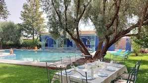 Ein Essbereich im Freien mit einem Tisch für vier Personen, umgeben von Stühlen, in der Nähe eines Pools und einem Gebäude mit blau-weißer Dekoration.