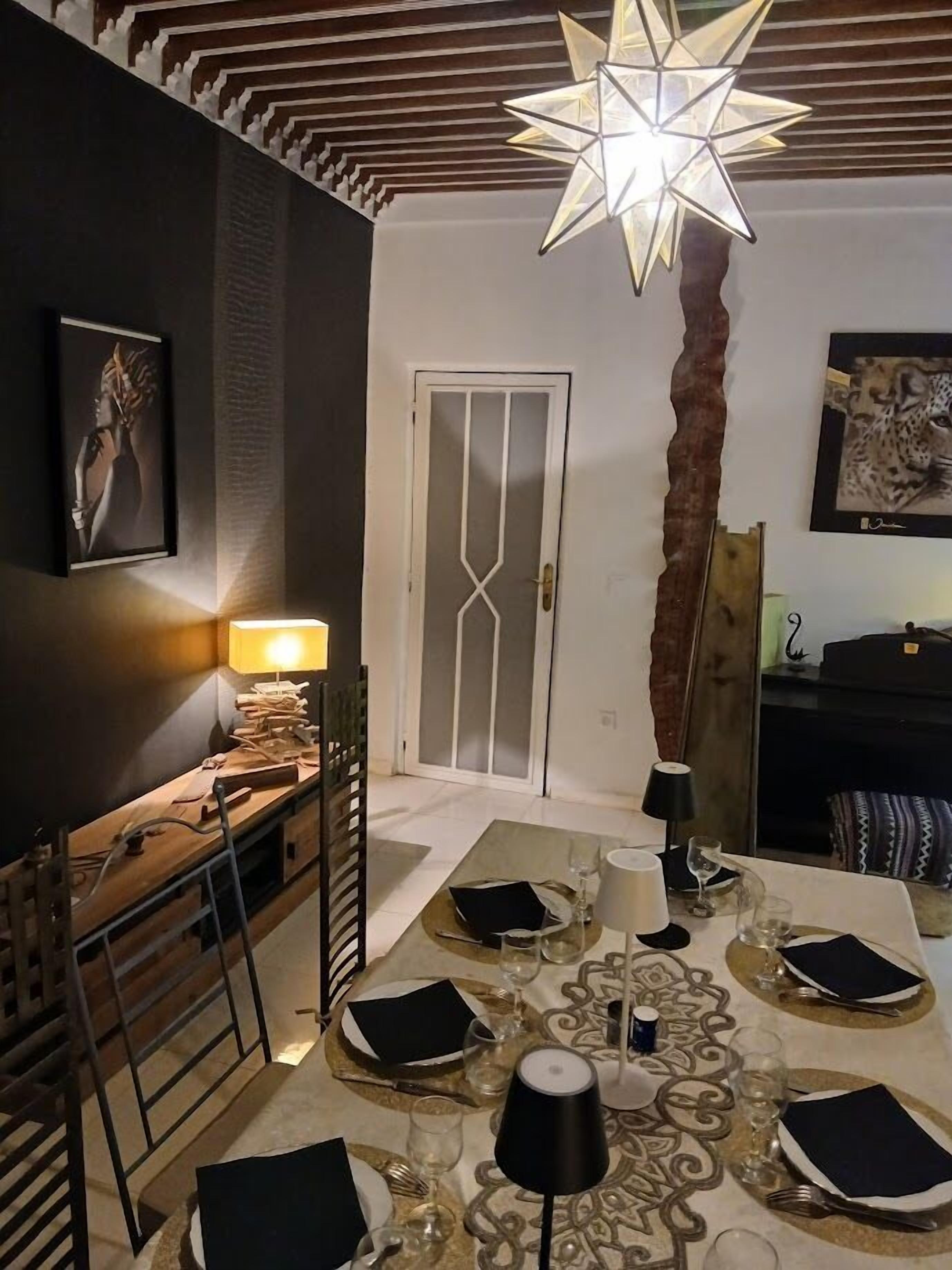 Un comedor con una lámpara en forma de estrella, una mesa de madera para cuatro personas y una puerta con diseño geométrico.