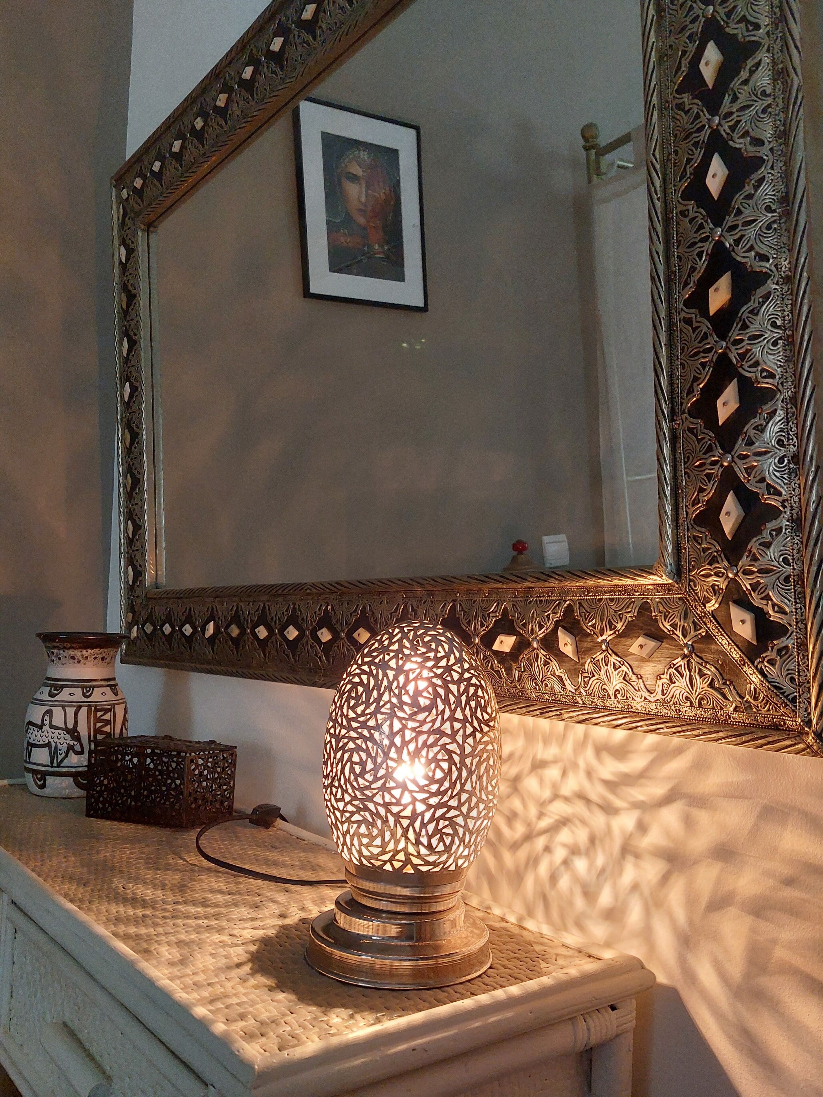 Une pièce décorée avec une lampe d’ornement, un tableau encadré au mur et un miroir aux motifs élaborés.
