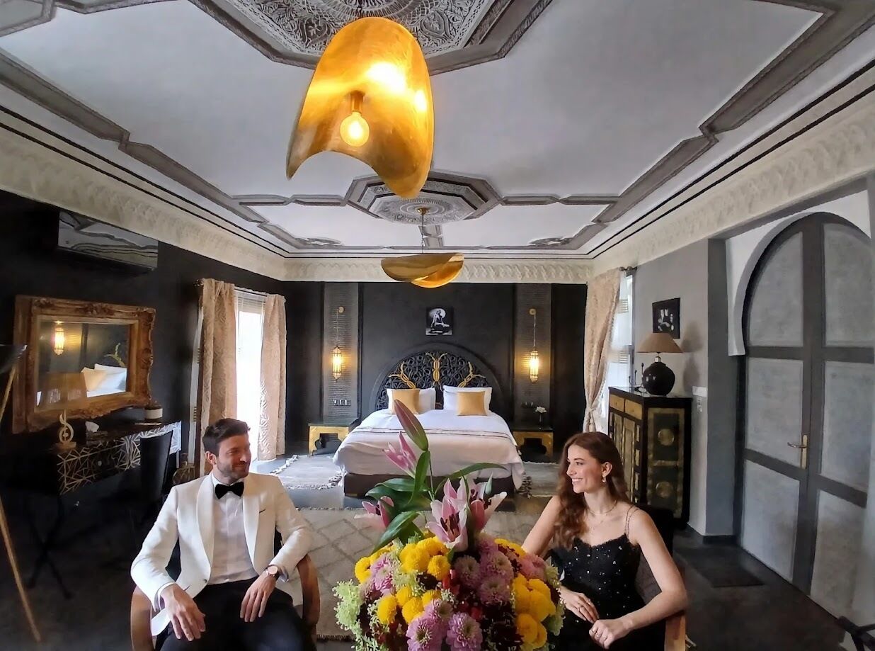 A hotel room with a large bed, a chandelier, and a decorative mirror.
