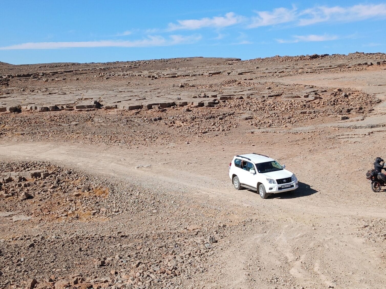 A white SUV on a dirt road in a rocky, barren landscape.
