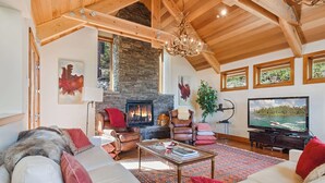 A spacious living room with a stone fireplace, leather armchairs, a large television, and a chandelier. - Luxury Mountain Retreat | Lake Views, Deck + BBQ | Pool Table & Chef’s Kitchen (Tahoe City)