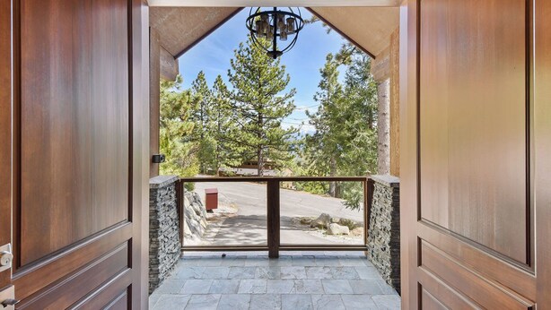 A wooden entrance with a stone wall and a view of trees and a road. - Luxury Mountain Retreat | Lake Views, Deck + BBQ | Pool Table & Chef’s Kitchen (Tahoe City)