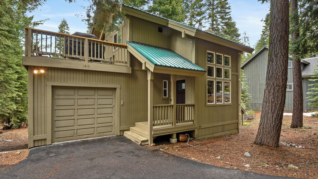 Une cabane en bois à deux étages, avec un toit vert, une véranda à l’avant et un garage.