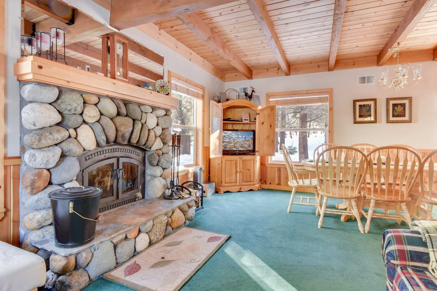 A cozy cabin interior with a stone fireplace, wooden dining table, and chairs.