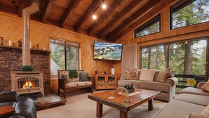 A cozy living room with a fireplace, leather sofas, a coffee table, and large windows offering a view of the outdoors.
